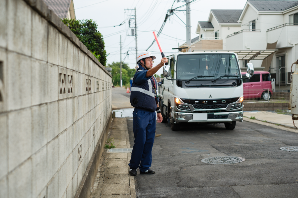 工事現場で歩行者の安全を確保するため交通誘導を行う警備員と作業車